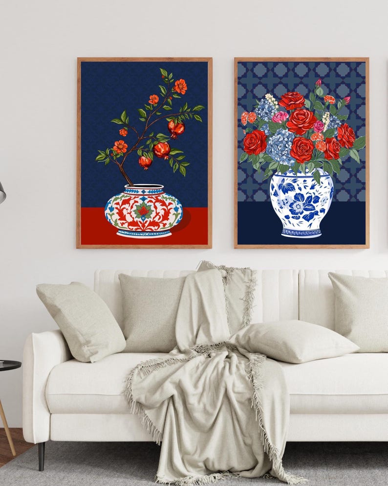 May include: Two framed wall art prints. The left print shows a pomegranate branch in a red and white patterned vase on a red surface. The right print features a bouquet of red roses and blue hydrangeas in a blue and white floral vase.