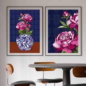 May include: Two framed wall art prints featuring vibrant pink peony flowers. The left print displays a blue and white floral vase with peonies on a brown surface. The right print shows a close-up of large pink peony blossoms against a dark blue background.