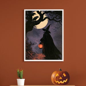 Peut inclure: Une impression d'art murale rectangulaire encadr&eacute;e repr&eacute;sentant une silhouette drap&eacute;e portant un chapeau pointu et tenant une lanterne orange lumineuse sur un chemin nocturne. La sc&egrave;ne montre une pleine lune, des arbres, des corbeaux et des chauves-souris.