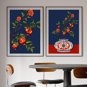 May include: Two framed wall art prints featuring pomegranate branches with red fruit and green leaves against a dark blue patterned background. One print shows a branch, while the other depicts a branch emerging from a decorative white and red vase.