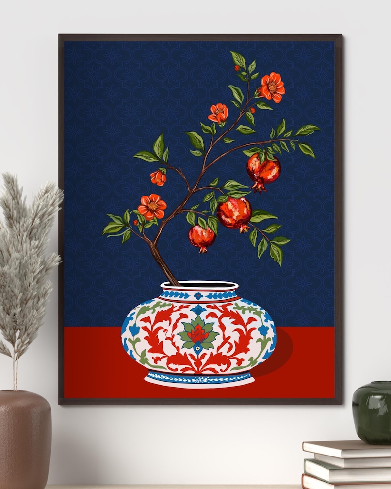 May include: A framed wall art print featuring a white ceramic vase with intricate red, blue, and green floral patterns. A pomegranate branch with green leaves, orange blossoms, and three red pomegranates emerges from the vase against a dark blue background.