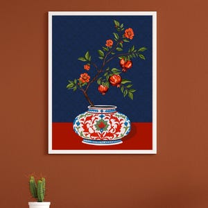 May include: A framed wall art print featuring a decorative ceramic vase with a white, red, and blue floral pattern. A pomegranate branch with green leaves, orange blossoms, and red pomegranate fruits emerges from the vase against a dark blue background.