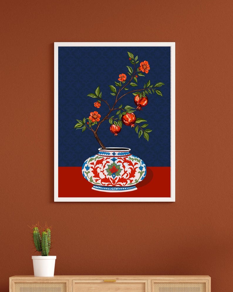 May include: A framed wall art print featuring a decorative ceramic vase with a white, red, and blue floral pattern. A pomegranate branch with green leaves, orange blossoms, and red pomegranate fruits emerges from the vase against a dark blue background.