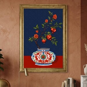 May include: A framed wall art print featuring a decorative vase with a white, red, and blue floral pattern. A branch with green leaves and several red pomegranate fruits extends upward from the vase against a dark blue background.