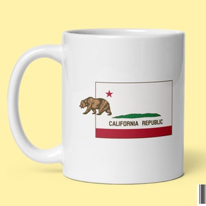May include: White ceramic mug with a graphic of the California state flag. The flag features a brown bear, a red star, and the words "California Republic".