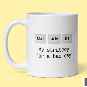 May include: White ceramic mug with a black and white design of computer keys labeled "Ctrl", "Alt", and "Del". The text below the keys reads "My strategy for a bad day".