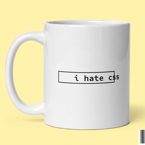 May include: White ceramic coffee mug with a black outline of a text box that says "i hate css".