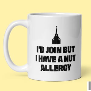 May include: White ceramic coffee mug with a black silhouette of a church and the text "I'd join but I have a nut allergy".