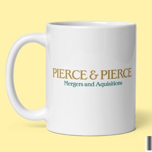 May include: White ceramic mug with a curved handle. The mug features the text "PIERCE & PIERCE" in gold lettering above the words "Mergers and Acquisitions" in green. The mug is on a yellow background.
