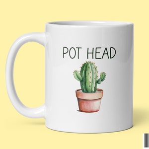 May include: White ceramic mug with a green cactus in a brown pot and the text "POT HEAD" in black.