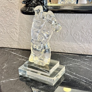 May include: A clear, transparent sculpture of a male torso, mounted on a tiered rectangular base. The sculpture is highly detailed, showcasing the musculature of the chest and abdomen. The base is also clear, creating a floating effect.