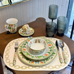 Op de afbeelding: Een eettafel met een theeservies met bloemmotief, borden en kommen. De set bevat een kop en schotel, een mok en een kom, allemaal met een bijpassend ontwerp. Ook inbegrepen zijn glazen, een vork, een mes en een lepel.