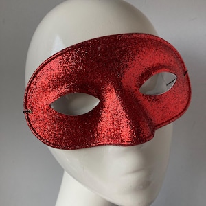 May include: A red glitter masquerade mask with a simple, elegant design. The mask has a wide, curved shape and covers the eyes.