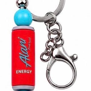 Puede incluir: Un llavero de metal con un dije cil&iacute;ndrico rojo que tiene el texto Alani ENERGY impreso en blanco y gris. El dije est&aacute; acentuado por dos cuentas esf&eacute;ricas de color turquesa brillante y dos cuentas de metal plateado m&aacute;s peque&ntilde;as en una argolla.