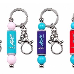 Puede incluir: Cuatro llaveros de metal con una pieza central cil&iacute;ndrica que lleva el texto Alani Energy. Cada llavero tiene un tubo central de color rosa, azul claro, morado o rojo, acentuado por dos cuentas redondas y una anilla plateada con mosquet&oacute;n.