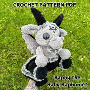 May include: Crochet pattern PDF for a gray and black amigurumi Baphomet with a pentagram on its forehead. The pattern is called "Baphly the Baby Baphomet".