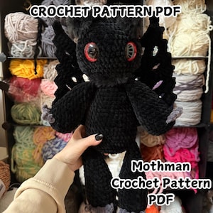 May include: A black crochet Mothman plush toy with red eyes and black wings. The toy is held in front of a shelf filled with yarn. Text on the image reads "CROCHET PATTERN PDF" and "Mothman Crochet Pattern PDF".