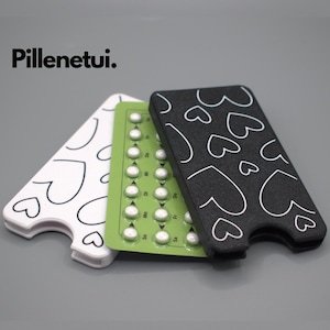 Op de afbeelding: Drie items: een witte hartvormige hoes, een groene pillenstrip en een zwarte hoes met witte hartcontouren. De tekst "Pillenetui." staat in de linkerbovenhoek. De pillenstrip staat in het midden, met zichtbare pillen.