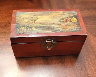 Petite boîte en bois vintage avec scène paisible peinte à la main. Quincaillerie en laiton, revêtement en laque ou en gomme laque. Bon état général. 6,75 po. × 3,5 po. × 3,25 po.