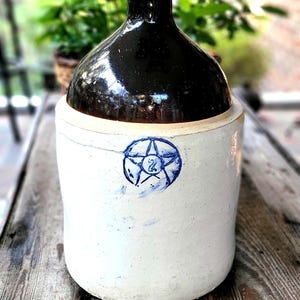 May include: A vintage stoneware crock with a brown glazed top and a white base. The crock has a blue star with the number "2" inside on the front.