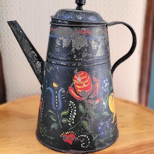Może przedstawiać: Czarny metalowy czajnik z malowanym wzorem kwiatowym w kolorze czerwonym, żółtym, niebieskim i zielonym. Czajnik ma czarny uchwyt i czarny guzik na pokrywce.