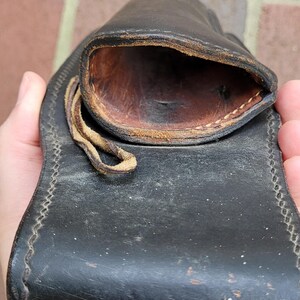 May include: A black leather pouch with a stitched border and a loop closure. The interior is a contrasting brown colour, and the leather shows signs of wear. The pouch is designed to hold small items.