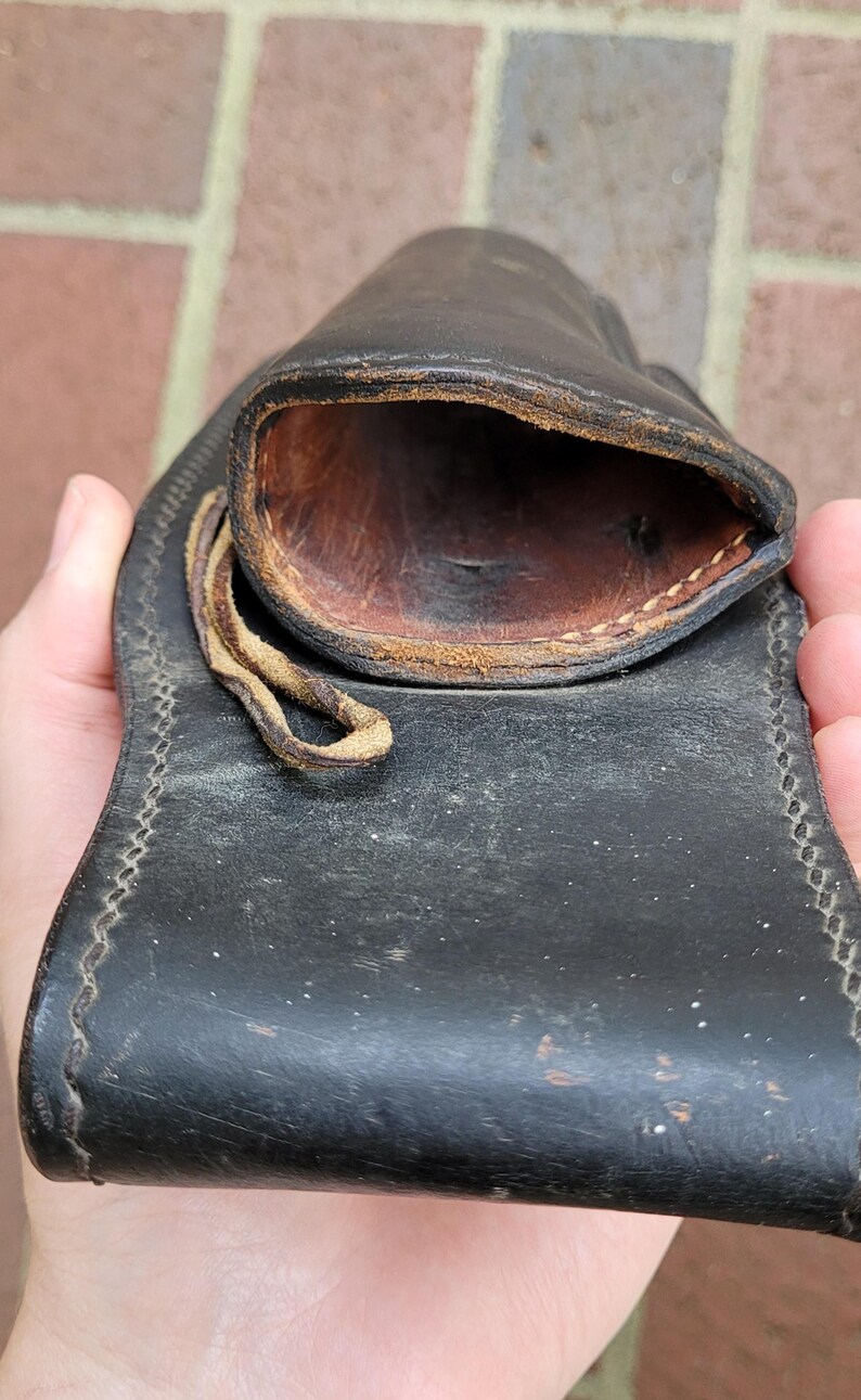May include: A black leather pouch with a stitched border and a loop closure. The interior is a contrasting brown colour, and the leather shows signs of wear. The pouch is designed to hold small items.