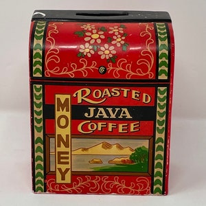 May include: Red wooden money box with a black top and a green and white border. The front of the box has a label that says "Roasted Java Coffee" and a picture of a mountain range and a lake. The box also has the word "MONEY" written vertically on the side.