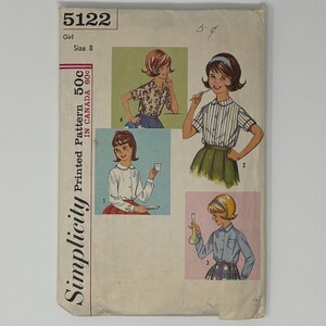 May include: Vintage Simplicity pattern envelope featuring illustrations of a girl in various outfits. The envelope is cream-colored with text and illustrations in red, black, and other colors. The pattern is for a size 8 girl.