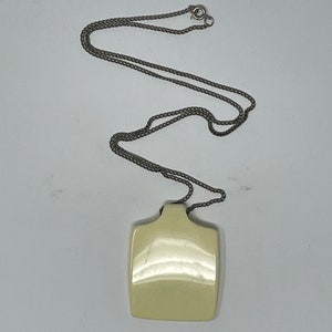 May include: A silver chain necklace with a square, off-white pendant. The pendant is smooth and shiny.