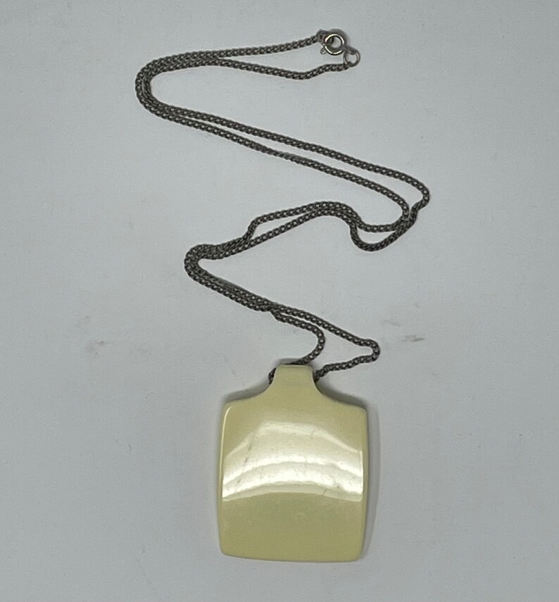 May include: A silver chain necklace with a square, off-white pendant. The pendant is smooth and shiny.