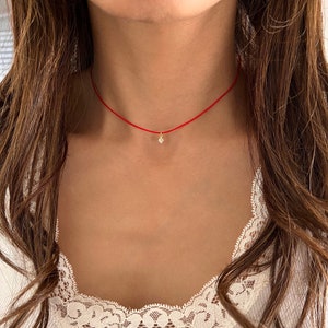 Könnte beinhalten: Eine rote Schnur-Halskette mit einem kleinen, klaren Edelstein-Anhänger.