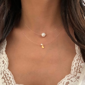 May include: A double-layered necklace featuring clear nylon cords. The top layer holds a single white pearl, while the bottom layer features a small white pearl paired with a tiny gold-toned heart charm, creating a delicate and layered appearance.