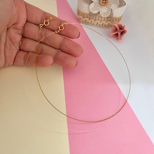 Könnte beinhalten: Eine goldene Kettenkette mit einem Verschluss. Die Kette ist dünn und zart und wird auf einem rosa und weißen Hintergrund gezeigt.