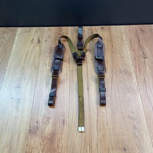 May include: Brown leather suspenders with a green canvas center strap. The suspenders have metal clips and are adjustable. The canvas strap has the text "MADE IN USSR" printed on it.