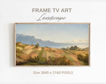 May include: A framed landscape painting of a field with a lake in the background. The field is divided into sections of different colors, including brown, green, and yellow. The lake is a light blue color and the mountains in the background are a dark blue color. The painting is in a wooden frame.