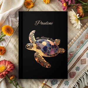 May include: A black journal with a gold-colored sea turtle illustration and the text "My Kintsugi Era" on the front cover. The name "Pauline" is written in a cursive font at the top of the cover.