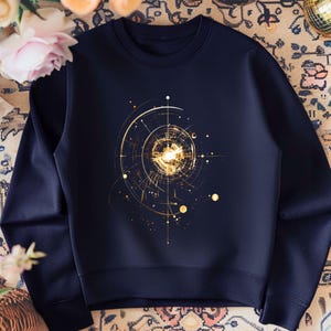Op de afbeelding: Marineblauwe sweatshirt met een gouden geometrisch ontwerp. Het ontwerp toont concentrische cirkels, lijnen en stippen. De sweatshirt is een crew neck stijl en lijkt gemaakt van een zacht materiaal.