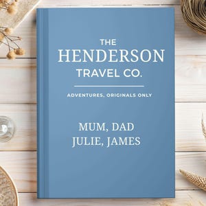 May include: A blue book with the text "THE HENDERSON TRAVEL CO." in white. Below it reads "ADVENTURES, ORIGINALS ONLY." The names "MUM, DAD JULIE, JAMES" are printed below. The book is on a light wood surface.