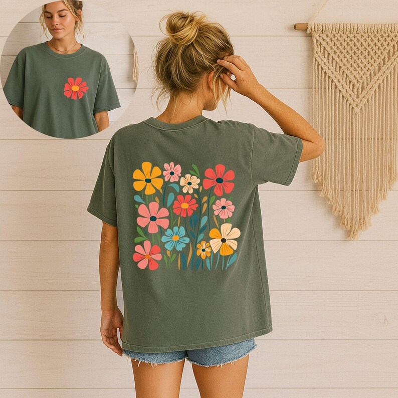 May include: An olive green t-shirt featuring a colorful floral design on the back and a single flower on the front. The floral design includes yellow, pink, red, and blue flowers with green leaves. The shirt is made of a soft material.