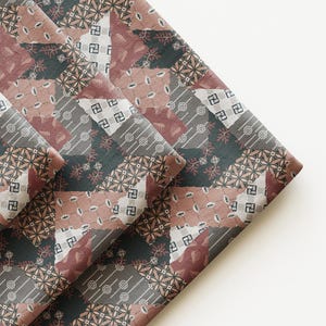 May include: A folded piece of fabric featuring a patchwork design with various geometric and floral patterns in shades of dark charcoal, muted mauve, and off-white. The textile displays repeating motifs including small circles, leaves, and squares.