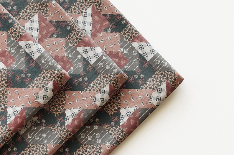 May include: A folded piece of fabric featuring a patchwork design with various geometric and floral patterns in shades of dark charcoal, muted mauve, and off-white. The textile displays repeating motifs including small circles, leaves, and squares.