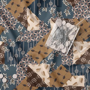 May include: A fabric featuring a patchwork design in shades of blue, brown, and cream with various floral and geometric patterns. A clear plastic container filled with white-headed sewing pins rests on the fabric, with two loose pins nearby.