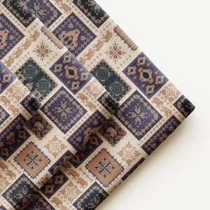 May include: Folded fabric featuring a repeating pattern of geometric shapes, including squares and diamonds, in shades of blue, brown, and beige. The design incorporates elephant and floral motifs, creating a textured, decorative appearance. The fabric is folded over on a white surface.