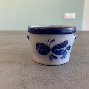 Op de afbeelding: Een klein, wit keramiek botervlootje met een blauwe rand en een blauw bloemenmotief. Het vlootje heeft twee kleine handvatten aan de zijkanten.