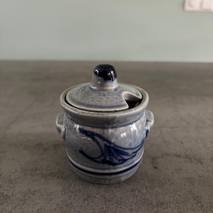 Op de afbeelding: Een klein blauw en wit keramiek suikerpotje met een deksel. Het potje heeft een blauw bloemenmotief en een tuit om te gieten.