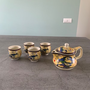 Peut inclure: Une théière jaune et quatre tasses à thé assorties avec un motif de dragon bleu. La théière a un couvercle et une poignée. Les tasses sont petites et n'ont pas de poignées.