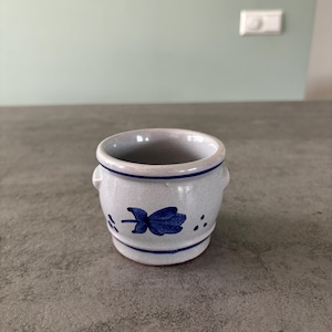 Könnte beinhalten: Ein kleiner, weißer Keramiktopf mit einem blauen Blumendesign. Der Topf hat eine abgerundete Form und einen leicht ausgestellten Rand.