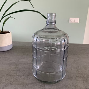 Op de afbeelding: Een heldere glazen fles met een getextureerd oppervlak. De fles heeft een brede opening en een ronde bodem.