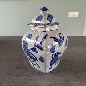 Może przedstawiać: Niebiesko-biały porcelanowy dzbanek na imbir z pokrywką. Dzbanek ma pękniętą glazurę i przedstawia wzór różnych przedmiotów, w tym czajnik, ptaka i krzesło.